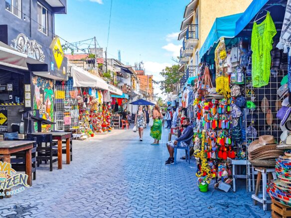 Expats and digital nomads walking down a street in Playa del Carmen lined with palm trees and apartment buildings, representing the best neighborhoods to live in the city.
